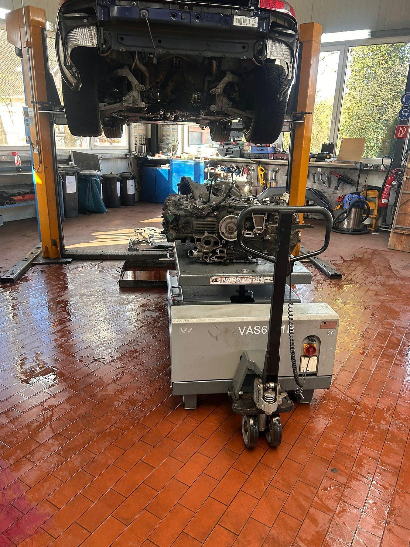 Fahrzeug auf der Hebebühne, darunter der ausgebaute Motor auf dem Hubtisch